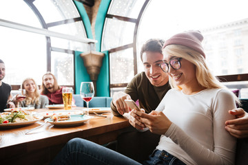 Young happy friends sitting in cafe chatting by phone.