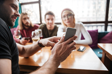 Attractive friends sitting in cafe and looking at phone.