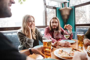Young happy friends in cafe eating pizza while drinking alcohol.