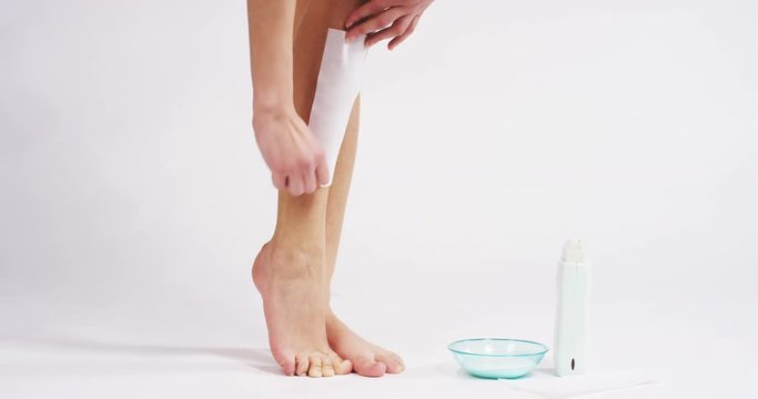 The young woman with perfect body doing depilation or her legs with waxing isolated on a white background. Concept of depilation, smooth skin, skincare, cosmetics, wellness center, healthy lifestyle