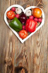 Vegetables. Peppers, tomatoes, garlic, onions, and radishes in the heart on rustic background