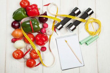 Naklejka na ściany i meble Sport and diet. Healthy lifestyle. Vegetables, dumbbells notebook. Peppers, tomatoes, garlic, onions radishes on a white background