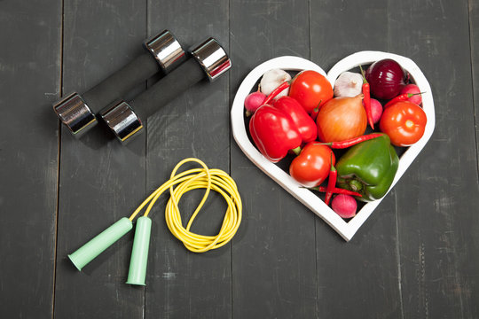 Sport and diet. Healthy lifestyle. Vegetables, dumbbells. Peppers, tomatoes, garlic, onion  radish in a heart on  black background
