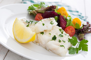 Fried cod fillet and salad in plate on white wooden background
