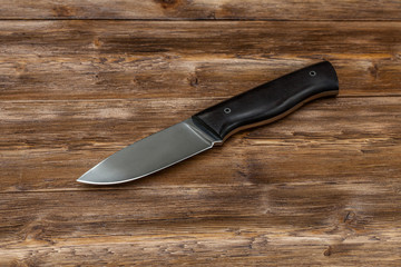 Hunting steel knife handmade on a wooden background, close-up