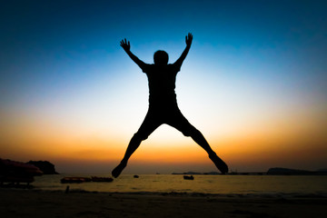 Back view of unidentified silhouette young man jumping over the sea beach with sunset background