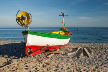 Fishing boat in colors of Italy on beach over blue sky. Noli, Liguria, Italy.
