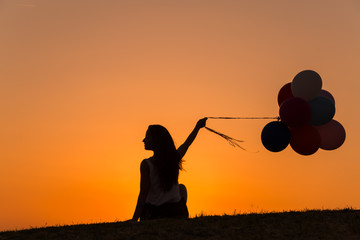 silhouette of a young woman playing with balloons at sunset