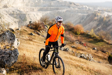 Cyclist in Orange Jacket Riding the Bike Rocky Hill. Extreme Sport Concept. Space for Text.