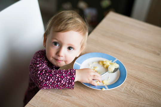 Cute Little Girl Sitting At The Table Eating Mashed Potatoes