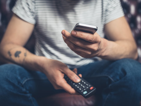 Man on sofa with phone and remote