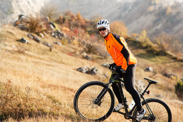 Fototapeta premium Cyclist in Orange Jacket Riding the Bike Rocky Hill. Extreme Sport Concept. Space for Text.