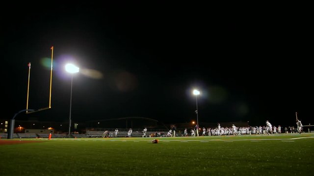 High school football team practicing in a stadium at night.