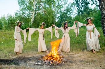 Four attractive Women with Wreath of Flowers dancing around bonfire. Ivan Kupala Holiday Celebration. Russia