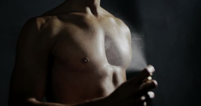 anonymous man spraying fragrance in extreme slow motion, with scent particles to wet skin after showering.