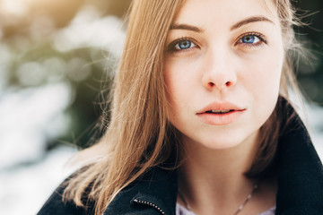 Closeup portrait beautiful blue eyes girl in black coat walking in winter park