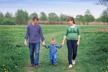 young family and young son walk on a spring meadow