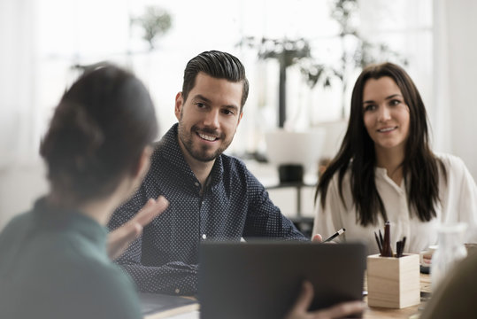 Smiling colleagues looking at businesswoman showing laptop during meeting