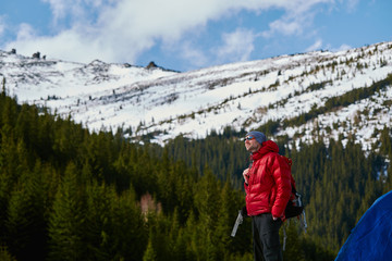 Fototapeta na wymiar hiker in red down jacket with backpack near the tent in the Carpathians mountains at winter