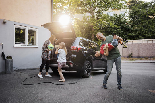 Playful Father And Son With Woman And Girl Standing By Car In Back Yard