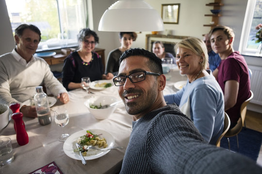Portrait of smiling man taking selfie with family and friends at dinner party