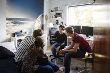 Young man showing smart phone to friends while sitting at bedroom