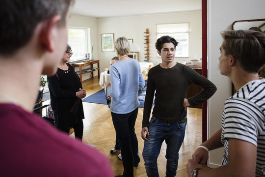 Multi-ethnic friends talking with family while standing in living room