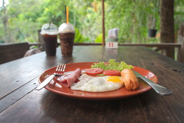Breakfast fried egg with ham and hotdog in a plate on the table.