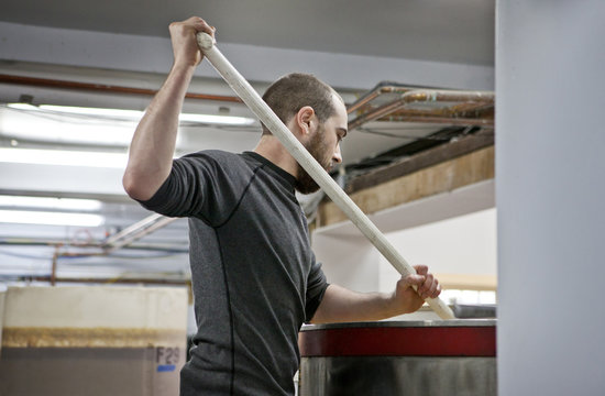 Distillery worker stirring in vat