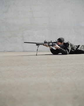Man aiming high powered rifle, in sniper position