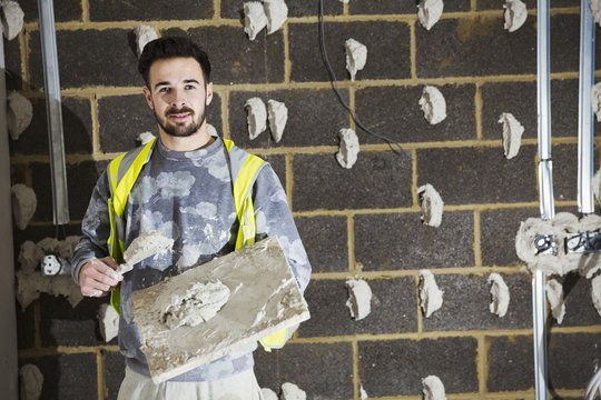 Plasterer with plasterboard and spreading trowel in front of cinder block wall