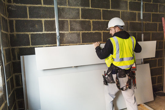 A workman in hard hat and high vis jacket stacking wood against a wall at a construction site. 