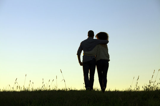 Rear view of young couple holding each other against background of clear evening sky
