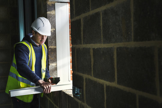A workman on a construction site, builder in hard hat using a saw on a plank of wood. 