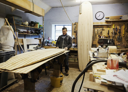 A surfboard workshop, a long board leant upright and a board in production on a workbench. Surfboard maker at work. - Powered by Adobe