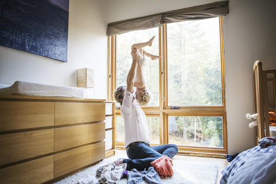 Father lifting son (18-23 months) in air in bedroom