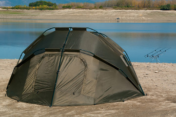 Landscape with fishing rods and hiking tent. Equipment for carp fishing with three fishing rods with reels on a support system - rod pod.