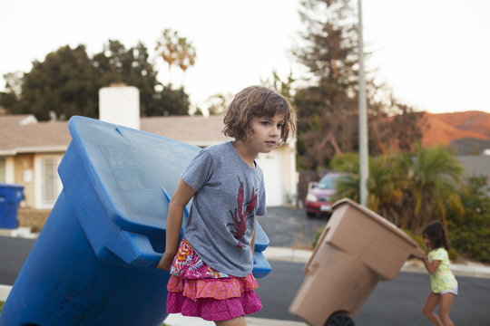 View of girl ( 8-9 ) pulling trash can