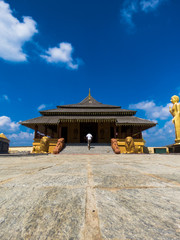 Obraz premium Man entering peaceful Golden Temple Palace Relic House on granite paved floor path Buddha Statues lion statue sclupture blue sky clouds at Nelligala International Buddhist Center Kandy, Sri Lanka