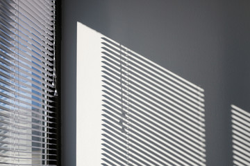 Sunlight and blinds creating shadow on a white wall, generic architectural detail.