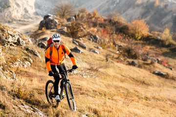 Cyclist in Orange Jacket Riding the Bike Rocky Hill. Extreme Sport Concept. Space for Text.