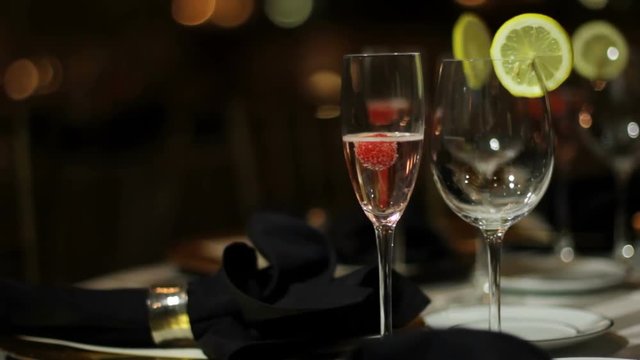 Tilt up of a glass of pink champagne and an empty water glass in a dark banquet hall.