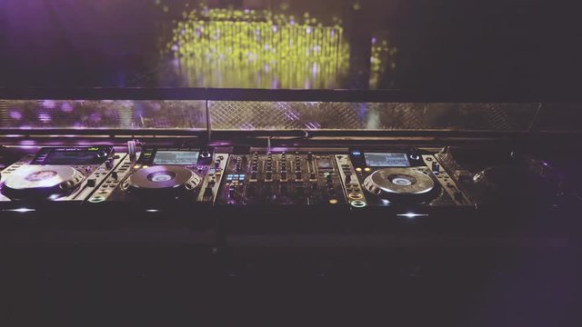behind dj decks and mixer in night club, static wide shot