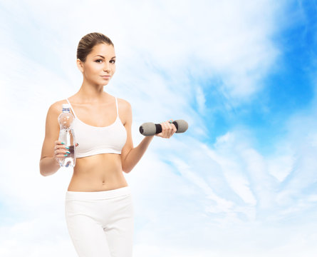 Young, sporty, fit and beautiful girl with the dumbbell over sky background. Healthy lifestyle and weight losing concept.