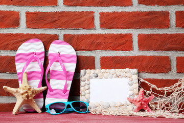 Frame of sea shells with starfish, flip-flops and sunglasses on brick wall background