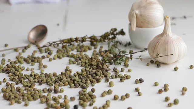Green peppercorns - pepe verde - famous spice of italian cuisine on white table with garlic bulbs, thyme twig and spoon. Pouring on white table. Selective focus.