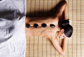 Beautiful, young and healthy woman on bamboo mat in spa salon is having hot stone massage. Spa,...