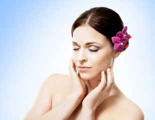 Close-up portrait of a beautiful girl with an orchid flower in her hair. Health, treatment, spa concept.