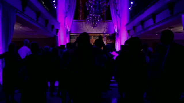 Group of silhouetted people dancing in a dark banquet hall for a wedding reception.