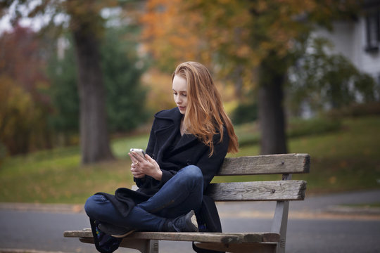 Young woman sitting on bench and using mobile phone